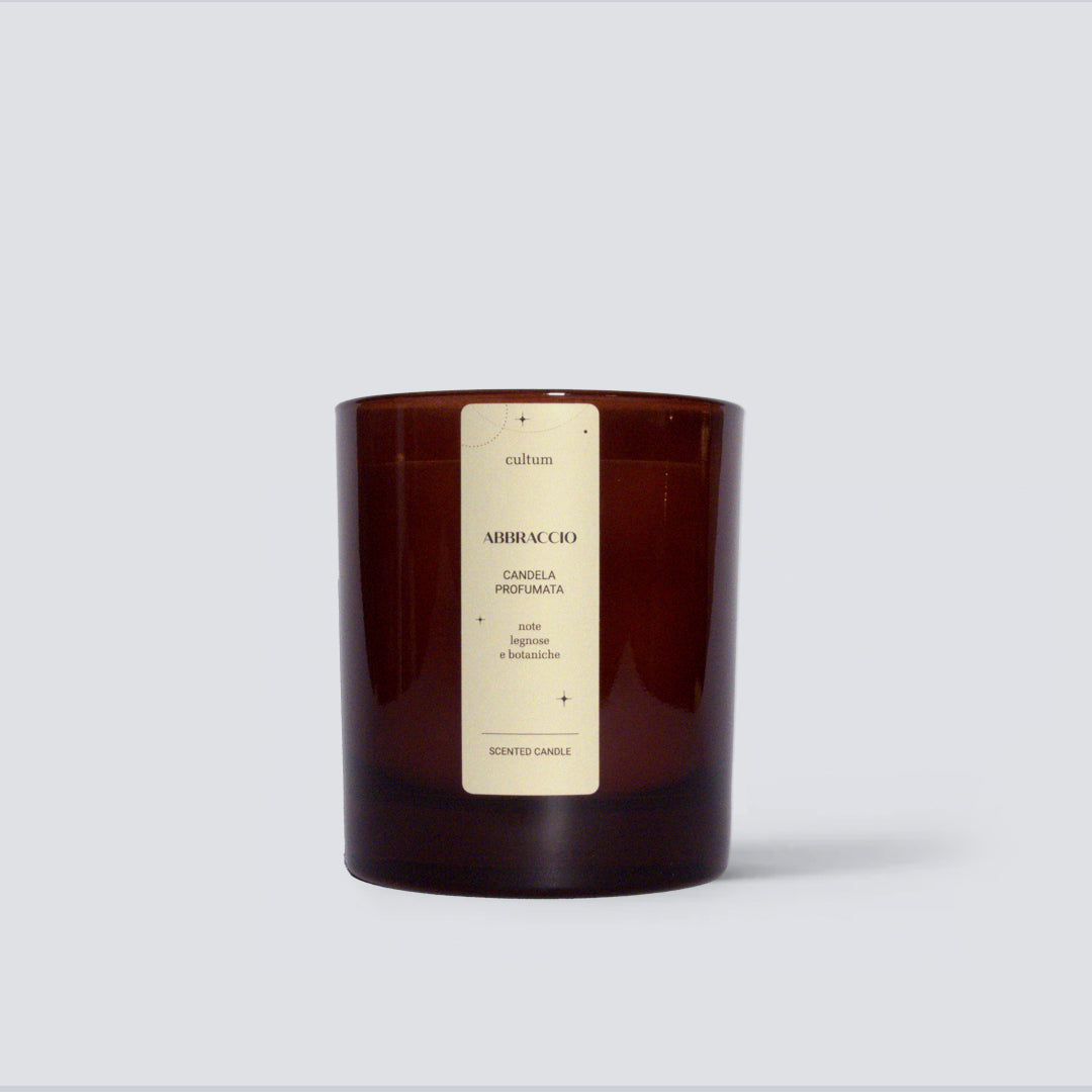 Candela profumata Cultum Abbraccio, posizionata su fondo chiaro con ombre morbide. Realizzata a mano con cera naturale. Fragranza botanica e legnosa con sfumature verdi e note calde, pensata per un ambiente accogliente, naturale e rassicurante.