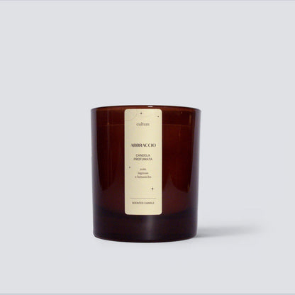 Candela profumata Cultum Abbraccio, posizionata su fondo chiaro con ombre morbide. Realizzata a mano con cera naturale. Fragranza botanica e legnosa con sfumature verdi e note calde, pensata per un ambiente accogliente, naturale e rassicurante.