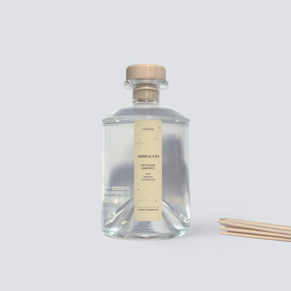 Diffusore ambiente Cultum Abbraccio con bastoncini in rattan, posizionato su piano chiaro con ombre morbide. Flacone minimal in vetro e fragranza botanica e legnosa, con sfumature verdi e note calde. I bastoncini in rattan rilasciano gradualmente il profumo, creando un ambiente accogliente, naturale e rilassante per la casa.
